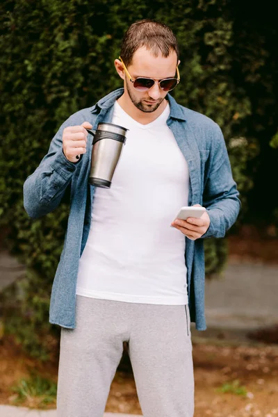 Beyaz tişörtlü adam telefon kullanıyor ve kahve içiyor. — Stok fotoğraf