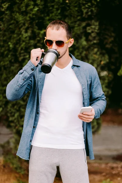 흰색 티셔츠를 입고 전화를 하고 커피 샘플을 마시는 남자 — 스톡 사진