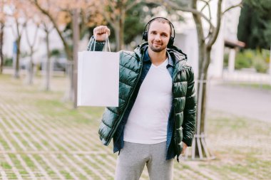 Beyaz kağıt çanta ve beyaz tişört modeli tutan bir adam.