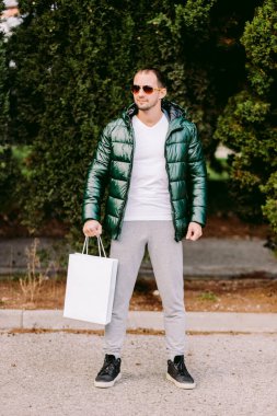 Beyaz kağıt çanta ve beyaz tişört modeli tutan bir adam.