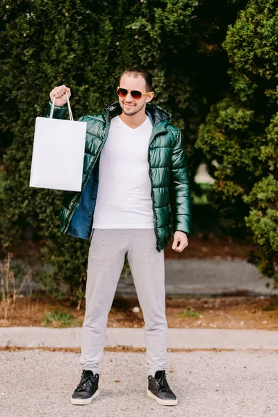 Beyaz kağıt çanta ve beyaz tişört modeli tutan bir adam. — Stok fotoğraf