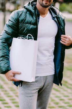 Beyaz kağıt çanta ve beyaz tişört modeli tutan bir adam.