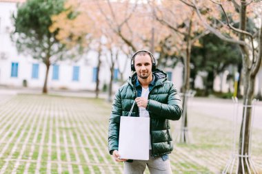 Beyaz kağıt çanta ve beyaz tişört modeli tutan bir adam.