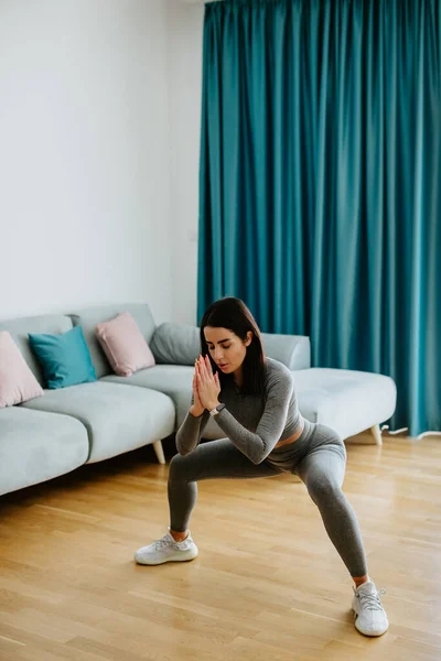 Giovane donna sportiva glutei squat routine di allenamento mattina in soggiorno Foto Stock