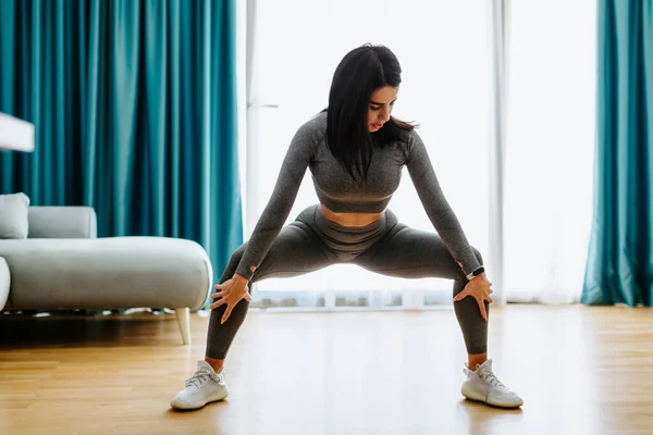Junge attraktive Frau praktiziert Yoga zu Hause. Dehnübungen der Beine Stockfoto