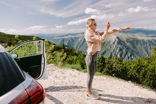 Glimlachende vrouw reizen met de auto in de bergen en het nemen van foto 's op de smartphone — Stockfoto