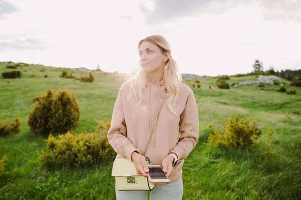 Güler yüzlü kız gün batımında kırsal alanda yeşil çayırda akıllı telefon kullanıyor. — Stok fotoğraf