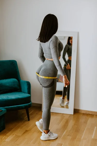 健康女人在家里用带子测量臀部。强壮的臀部. — 图库照片