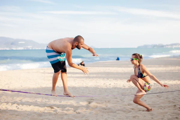 Teenage par balansera slackline på stranden — Stockfoto