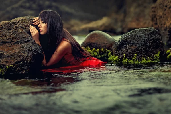 Brunette lady in red dress in the water between rocks — Stock Photo, Image