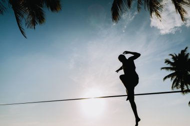 teenage jumping on slackline with sky view clipart