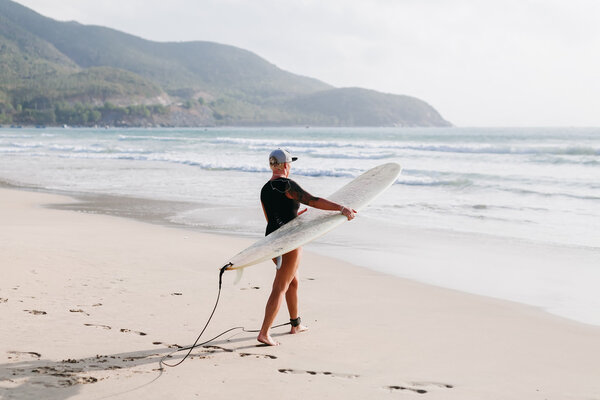 женщина с доской для серфинга на пляже
