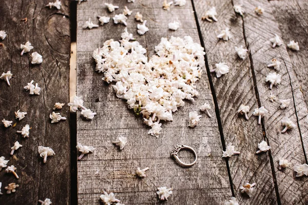 Нежные белые цветы в форме сердца с кольцом на деревянном столе — стоковое фото