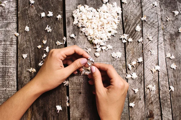 Anillo de boda en las manos y corazón blanco de flores fondo — Foto de Stock