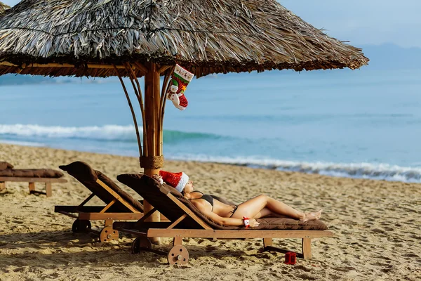 Санта дівчина в бікіні лежить на сонячному ліжку на пляжі — стокове фото