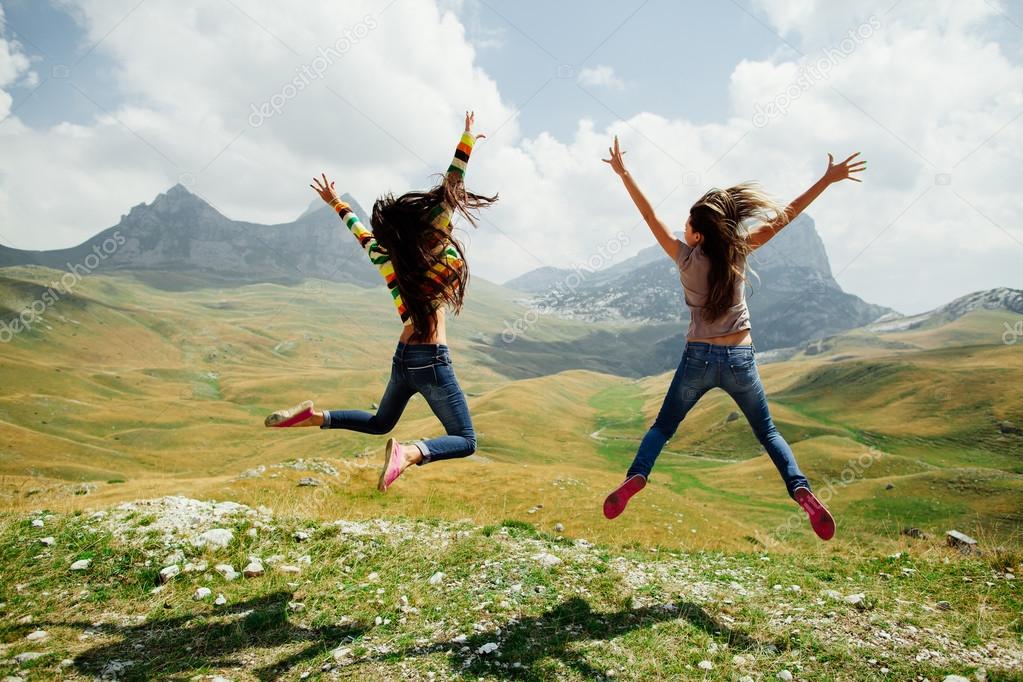two girls happy jump in mountains with exciting view