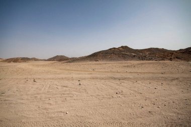 Arkasında dağlar ve piramitler olan güneşli kumlu bir çöl manzarası