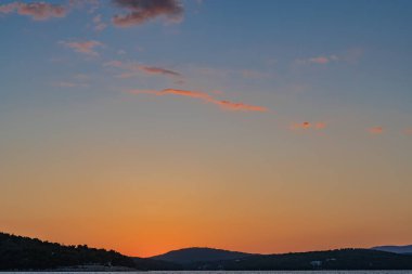 Güneş deniz ufkunun hemen üstünde kayalık plajların panoramasıyla bir gündoğumu / günbatımı yaratıyor.