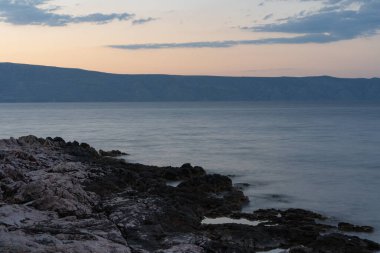 Güneş deniz ufkunun hemen üstünde kayalık plajların panoramasıyla bir gündoğumu / günbatımı yaratıyor.