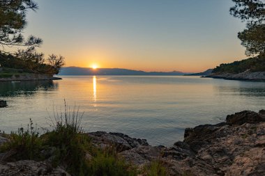 Güneş deniz ufkunun hemen üstünde kayalık plajların panoramasıyla bir gündoğumu / günbatımı yaratıyor.