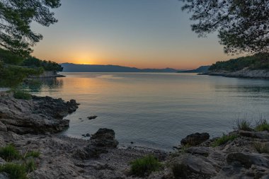 Güneş deniz ufkunun hemen üstünde kayalık plajların panoramasıyla bir gündoğumu / günbatımı yaratıyor.