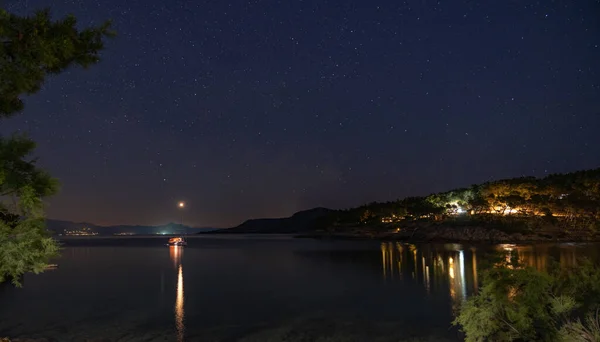 Night view of the very calm sea on the shore with the illuminated town in the background