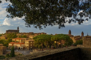 Toskana çatıları, çan kuleleri, gün batımı ışığı, avlu, ağaç örtüsü, köy cazibesi, yaz günü.