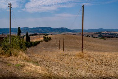 Kuru kahverengi tarlaları geçen elektrik direkleri yaz mevsiminde gökyüzünün altındaki uzak mavi tepelere doğru ilerliyor..