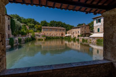 Gölgeli taş pencere tarihi Toskana spa havuzunu gösteriyor. Kırsal hamamlar ve ağaçlar yansıyor..