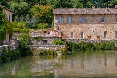 Tarihsel taş kaplıca binası ve bereketli yeşilliklerle çevrili duvarlar yaz havuzu suyuna yansıyor..