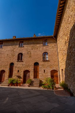 Geleneksel taş binalar ve kapılar sessiz bir avluda, Pienza 'da mavi gökyüzünün altında güneşleniyorlar..
