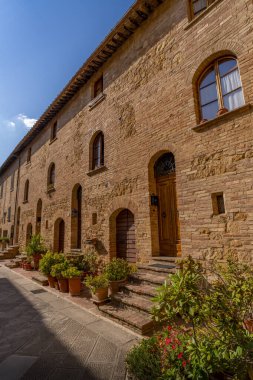 Geleneksel taş binalar ve kapılar sessiz bir avluda, Pienza 'da mavi gökyüzünün altında güneşleniyorlar..