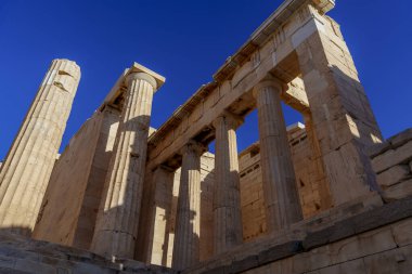 Atina 'daki Akropolis' te Propylaea 'nın heybetli mermer sütunları ve anıtsal girişi, açık mavi gökyüzü ile tezat oluşturuyor.