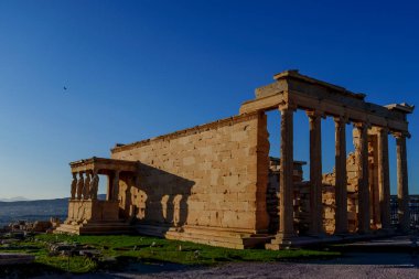 Antik Erechtheion tapınağı sıcak öğleden sonra ışığında yıkandı, Akropolis platosunda uzun gölgeler bıraktı..