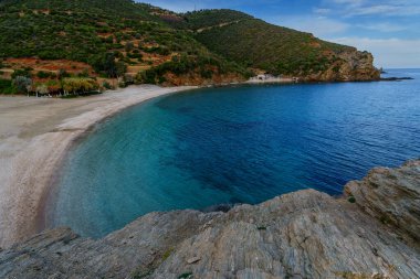 Boş hilal plajı, yeşil tepelerin ve kayalık burunların altındaki derin mavi körfezin sınırında..