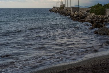 Yumuşak dalgalar bulutlu gökyüzünün altında dalgalı bir dalganın yanında çakıllı bir kıyıya yuvarlanıyor..