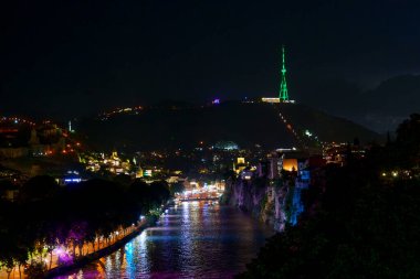 Mtatsminda TV kulesi Tiflis 'in üzerinde yeşil parlarken, nehir kenarındaki renkli ışıklar Kura Nehri' ni yansıtıyor..