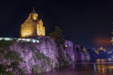 Taş kilise sarp kayalıkları taçlandırır, ılık ışıkları karanlık, yavaşça akan nehri yansıtır..