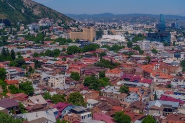 Renkli eski Tiflis çatıları açık mavi bir gökyüzü altında modern yüksek binalara ve dağlara doğru yeşil bir vadiye yayıldı..