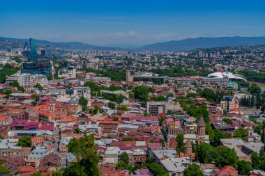 Renkli Eski Tiflis çatıları, kiliseler ve yeşil parklar modern ufuk çizgisi ve çevre dağlarla tezat oluşturuyor.