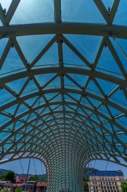 Tekrarlayan çelik kemerler ve mavi cam paneller şehrin yayaları üzerinde bir ışık tüneli oluşturur..