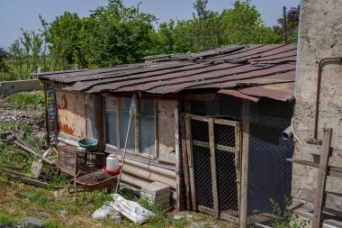 Paslı metal çatılı, yıpranmış kır kulübesi ve ekili tavuk kümesi.