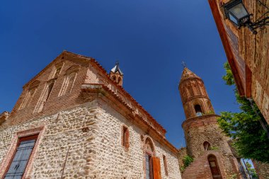 Silindirik çan kulesiyle tarihi tuğla kilise cephesi bulutsuz mavi gökyüzünün altında yeşilliğin üzerinde yükseliyor.