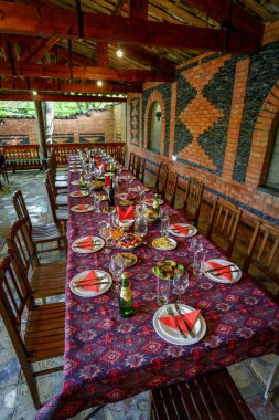 Renkli masa örtüsü, düzenlenmiş tabaklar, bardaklar ve tabaklar açık tuğla köşkte misafirleri bekliyor.