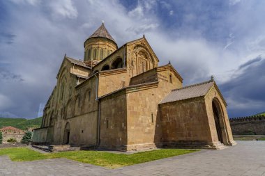 Fırtınalı bulutlara karşı güneş ışığıyla aydınlatılan uzun kubbeli tarihi Gürcistan katedrali.