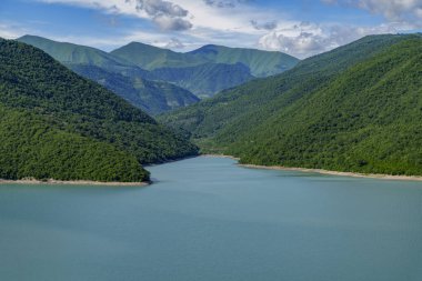 Sakin turkuaz rezervuar uzak katmanlı dağ sırtları ile ormanlık tepeler arasında dönüyor.