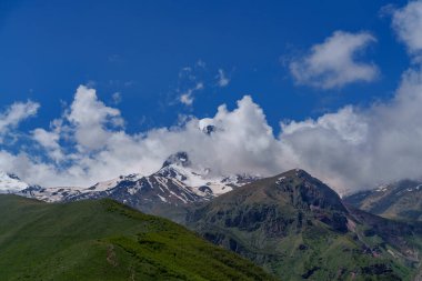Gürcistan 'daki ikonik Kazbek Dağı parlak mavi gökyüzünün altındaki yemyeşil tepelerin üzerinde yükseliyor.