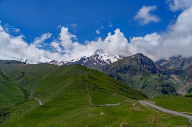 Gürcistan 'da dolambaçlı dağ yolu olan yemyeşil bir vadi üzerindeki Karlı Kazbek Dağı kuleleri..