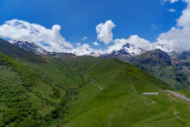 Gürcistan 'da dolambaçlı dağ yolu olan yemyeşil bir vadi üzerindeki Karlı Kazbek Dağı kuleleri..