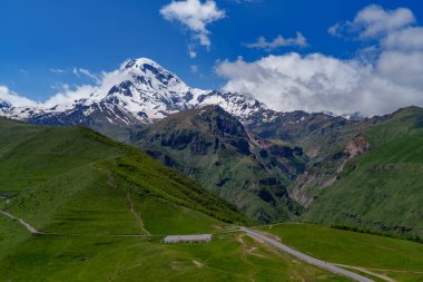 Gürcistan 'da dolambaçlı dağ yolu olan yemyeşil bir vadi üzerindeki Karlı Kazbek Dağı kuleleri..